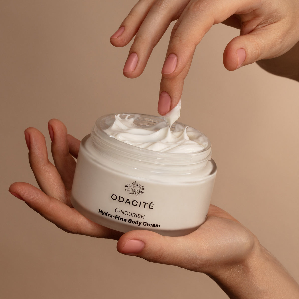 Main prélevant une dose de C-Nourish Crème Corps Hydra-Firm de Odacité. Double dose de vitamine C