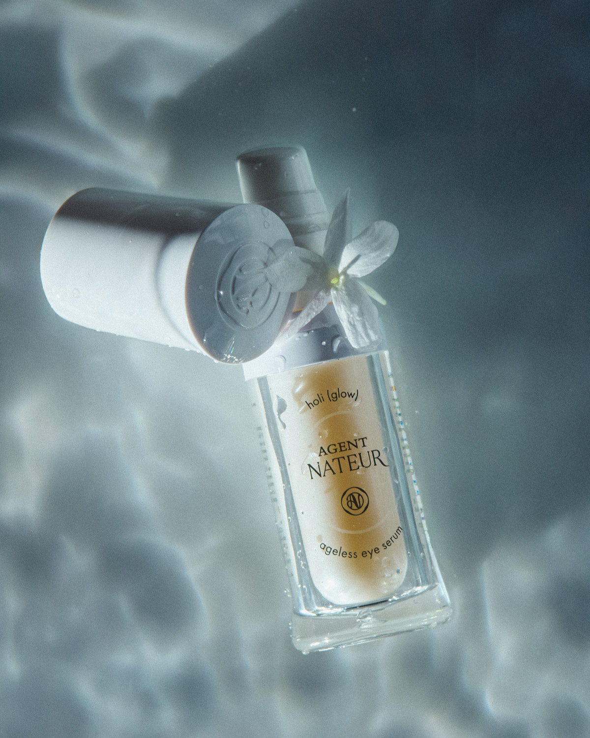 Holi (Glow) : Ageless Eye Serum - Agent Nateur - flacon ouvert surmonté d'une fleur blanche