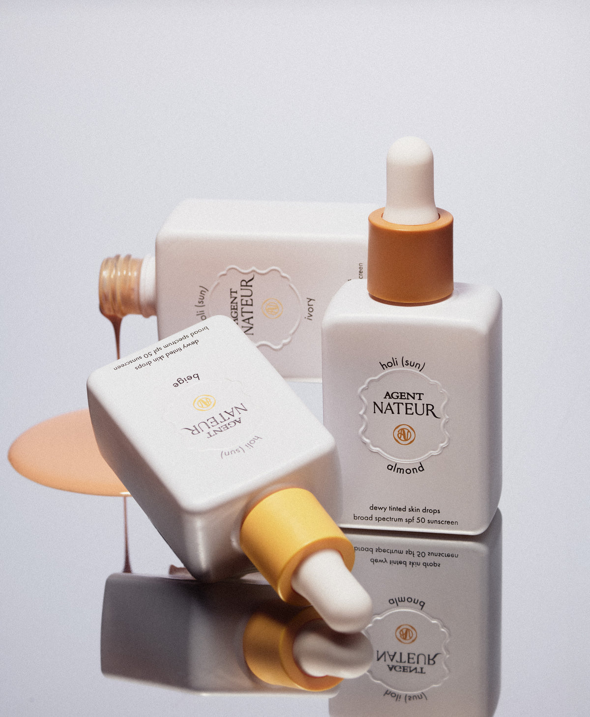 Holi (Sun) Dewy Tinted Skin Drops SPF50 - Agent Nateur - trois flacons empilés et coulée de teinte